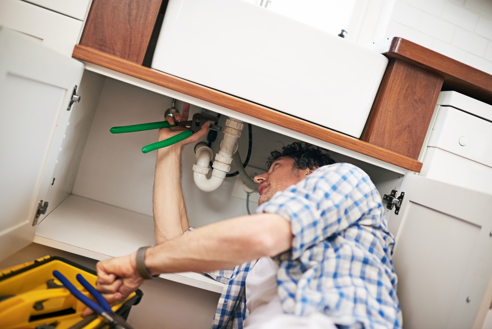 DIY homeowner fixing a pipe under his kitchen sink.